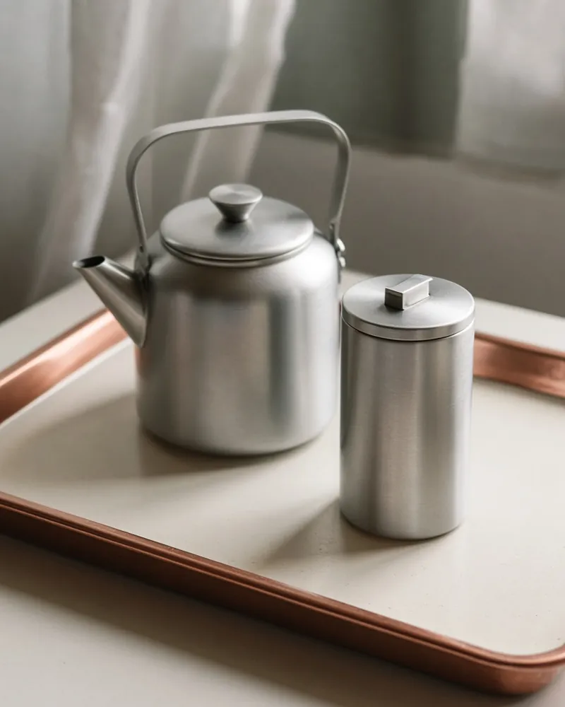 A plain kettle and a small hot-water carafe on an enamel counter, handles visible.